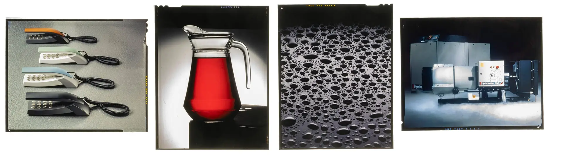 A collection of four large-format 5x4 inch film transparencies arranged on a Lightbox. The transparencies show high-end studio product shots: a glass pitcher of red liquid, water droplets on a dark surface, a row of four colourful telephones, and a shot of compressors with dry ice